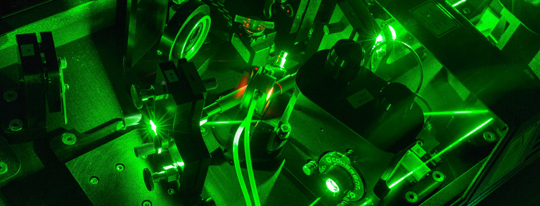 Eine Detailaufnahme eines Lasers im Labor in dunkel grünen Farben.